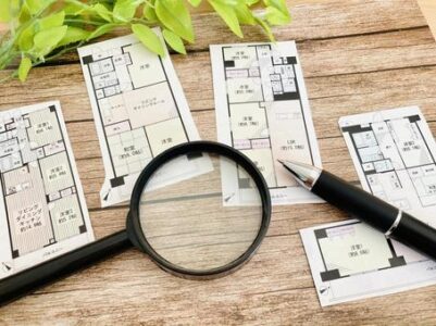 Architectural floor plans spread on a wooden table with a magnifying glass and a pen for inspection or planning.] ,