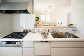 Bright white kitchen with a gas stove, double sink, and an island, opening to a sunny dining area in the background.