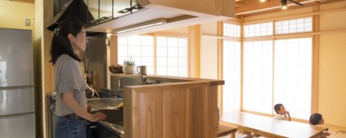 木のキッチンに立つお母さんと、座卓で過ごす子どもたち